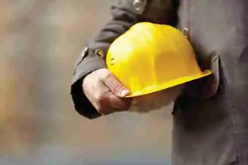 Worker stands holding yellow hard hat